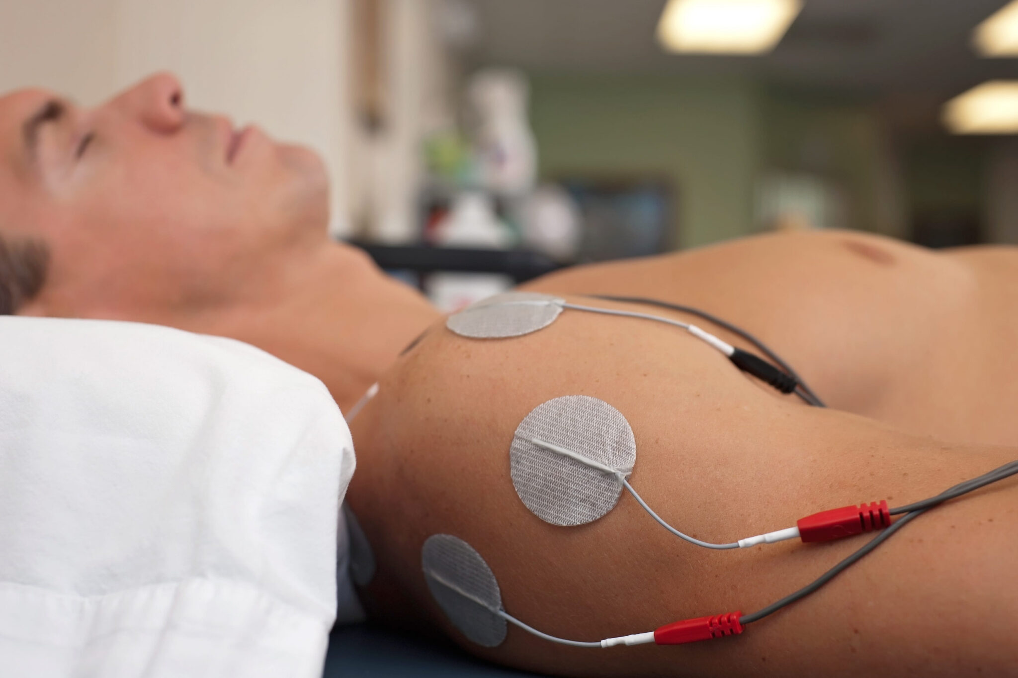 Physical therapy or chiropractic treatment of a male patient's injured shoulder using transcutaneous interferential electrical stimulation (TENS) for pain management.